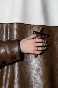 Detalle del gesto de la mano sujetando el crucifijo